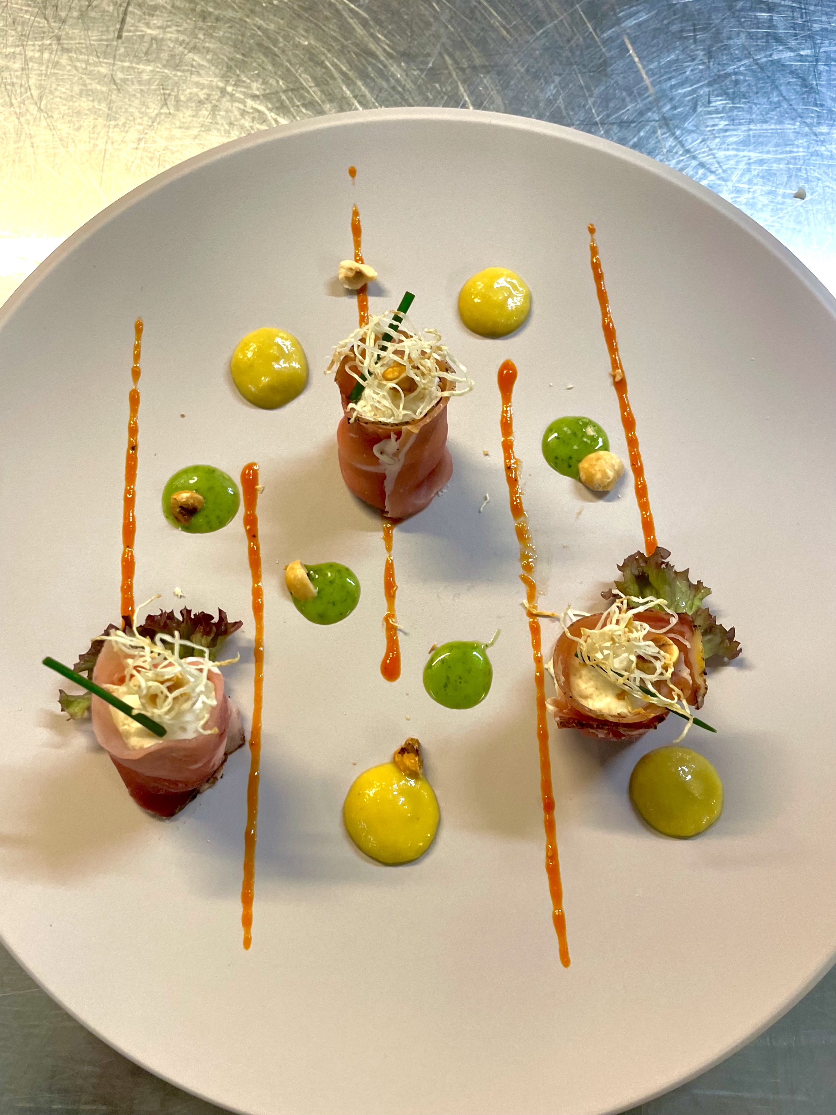 Cannoli di speck ripieni di mousse di yogurt, rafano e pinoli, salsa al peperone, pesto di rucola e sedano rapa fritto.